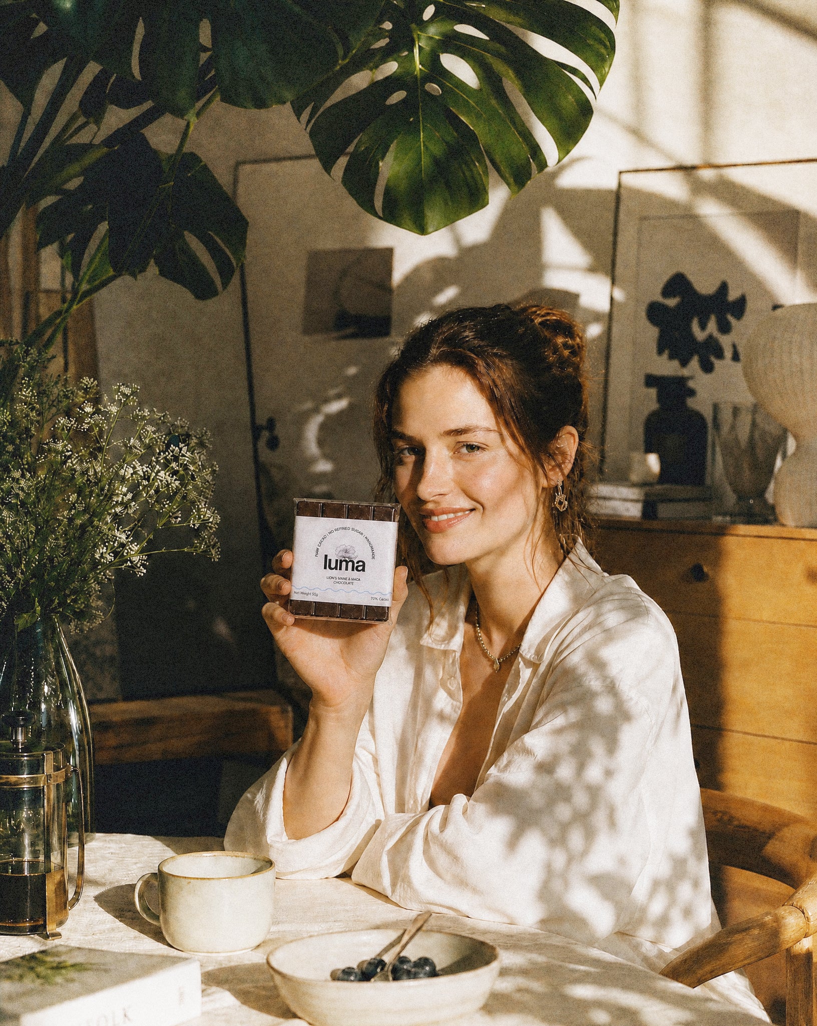 Woman holding luma mushroom chocolate with lion's mane in a cozy indoor setting with plants and decor.
