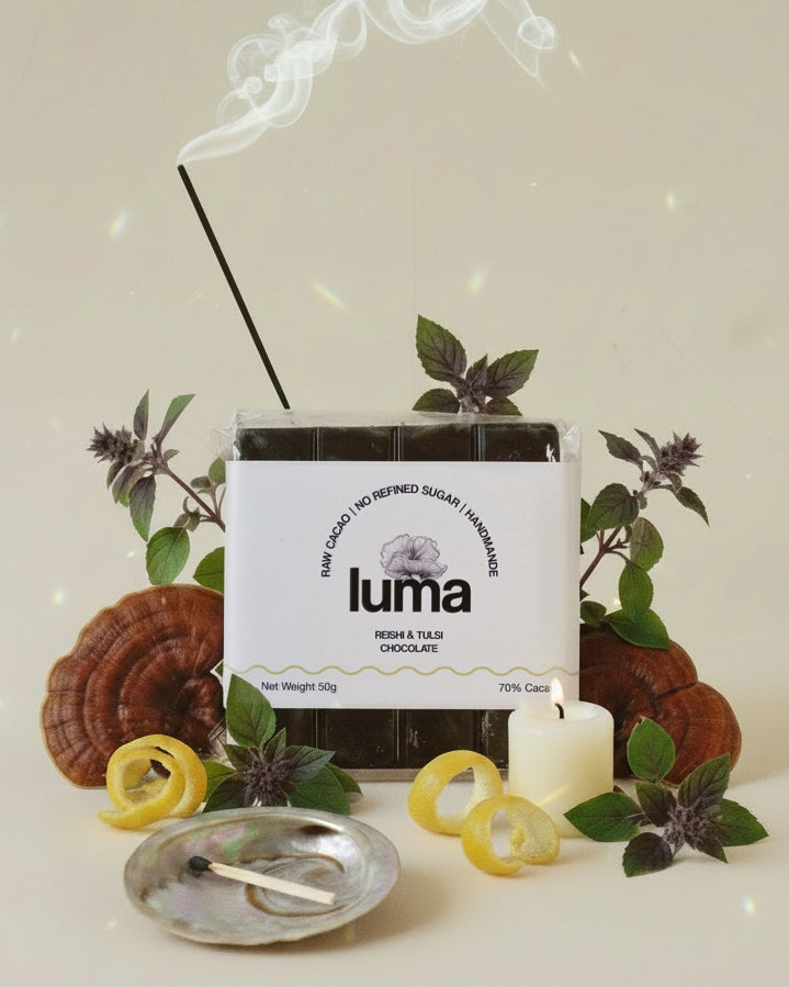 luma reishi and tulsi chocolate packaging surrounded by fresh reishi, tulsi, lemon zest, a candle, burning incense and shell with a match
