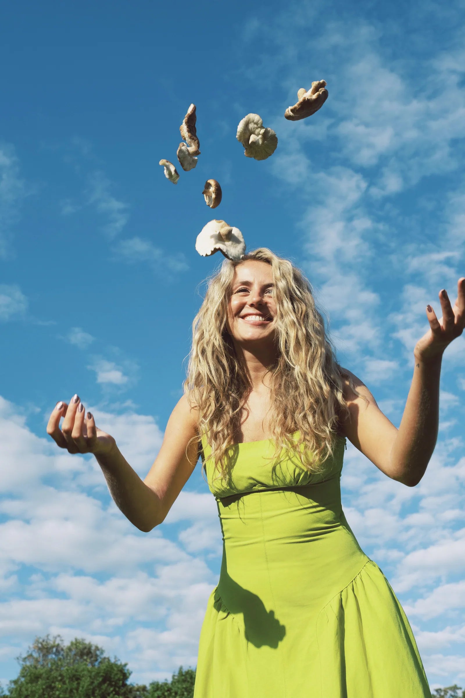 A smiling person tossing Shiitake mushrooms into a blue sky.